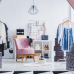 Pink chair in dressing room with flowers on designer table and clothes on hangers. Fashionable dressing room concept